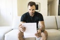 Depressed mature man holding paper and looking at it while sitting on the couch at home Royalty Free Stock Photo