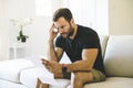 Depressed mature man holding paper and looking at it while sitting on the couch at home Royalty Free Stock Photo