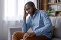 Depressed mature senior gray haired man sitting sad alone by window on couch in living room, african american frustrated Royalty Free Stock Photo