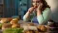 Depressed obese female eating carrot instead donut and fast food, dieting