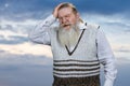 Depressed old bearded man touching his head on cloudy sky background. Royalty Free Stock Photo