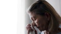 Depressed old lonely woman wiping tears with tissue while looking through the window Royalty Free Stock Photo