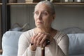 Depressed old woman sitting on couch, leaning on cane