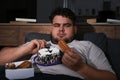 Depressed overweight man eating sweets in room at night Royalty Free Stock Photo