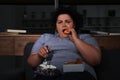 Depressed overweight woman eating sweets in room at night Royalty Free Stock Photo