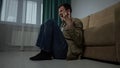 Depressed sad man with hugging the knees sits on floor near sofa in living room. Royalty Free Stock Photo