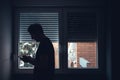 Depressed sad man using mobile phone in dark room by the window with shutters pulled down Royalty Free Stock Photo