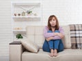 Depressed and sad middle aged woman sitting with clamped knees on bed, coach, sofa at home. Copy space and mock up. Royalty Free Stock Photo