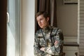 Depressed and sad soldier in green uniform with trauma after war standing near the window Royalty Free Stock Photo