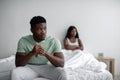 Depressed sad young black man ignores offended lady after quarrel sits on bed in bedroom interior, copy space Royalty Free Stock Photo