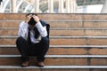 Depressed stressed young Asian business man in suit with hands on head sitting on stairs. Unemployment and layoff concept