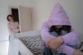 Depressed teen girl wearing hood sitting on bed ignoring mother Royalty Free Stock Photo