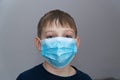 Depressed unhapped boy in blue medical mask in coronavirus COVID19 quarantine at home. Epidemic control of coronavirus infection.