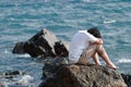 Depressed upset young Asian man covering face with hands sitting on the rock of sea shore Royalty Free Stock Photo