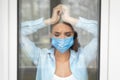 Depressed Woman Standing Near Windor At Home, Wearing Protective Mask Royalty Free Stock Photo