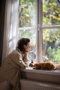 Depressed woman thinking about troubles sadly looking at window curious cat trying support owner. Royalty Free Stock Photo
