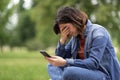 Depressed Young Arab Woman Sitting Outdoors With Smartphone In Hands And Crying