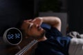 Depressed young Asian man lying in bed cannot sleep from insomnia. focus on clock