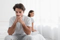 Depressed young caucasian husband with stubble sits on bed and sad, ignoring offended lady in bedroom Royalty Free Stock Photo