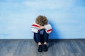 A depressed young guy in a white sweater with a rainbow pattern sits leaning against the blue wall, hugging knees, Royalty Free Stock Photo