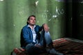 Depressed young man sitting on a mattress in a dark prison cell