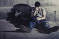 Depressed young man sitting on street ground with shadow on concrete wall