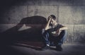 Depressed young man sitting on street ground with shadow on concrete wall