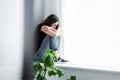 depressed young woman crying while sitting on window sill and hiding face in crossed arms. Royalty Free Stock Photo