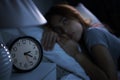 Depressed young woman lying in bed cannot sleep from insomnia. Selective focus on alarm clock Royalty Free Stock Photo