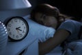 Depressed young woman lying in bed cannot sleep from insomnia. Selective focus on alarm clock Royalty Free Stock Photo