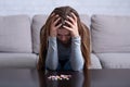 Depressed young woman sitting head in hands near pile of tablets, planning to commit suicide at home