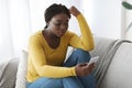 Depression Concept. Upset Black Lady Sitting Lonely At Home Looking At Smartphone Royalty Free Stock Photo