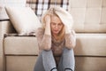 Middle aged barefoot woman sitting at the floor embracing her knees, near sofa at home, her head down, bored, troubled Royalty Free Stock Photo