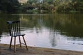 Depressive dark concept of loneliness with showing empty chair near lake and forest in the evening Royalty Free Stock Photo