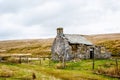 Derelict abandoned building, cottage, with crumbling walls and roof on grass with a blue sky.