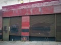 Derelict abandoned store with shuttered vandalized shop front with peeling red paint on an urban street