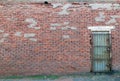 Derelict old shabby industrial building with a cracked and patched brick wall and a padlocked rusty metal door with steel bars Royalty Free Stock Photo