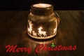 A derivative glowing candle glass in the dark with reindeer on it and the lettering Merry Christmas