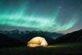 Nighttime mountain view featuring illuminated tent under starry sky with long exposure effect. Royalty Free Stock Photo