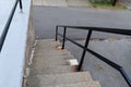 Descending flight of exterior concrete stairs with recently painted black pipe railing, narrow steps to street level
