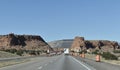 A Desert Highway Cuts Through Two Red Rock Formations With a Mountain in the Background