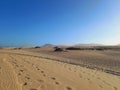 Desert landscape and dunes with footprints in the sand under blue sky and volcanoes on the horizon. Nature and extreme sports Royalty Free Stock Photo
