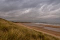 A deserted Embleton Bay in Northumberland, England, through the marram grass with cloudy skies overhead