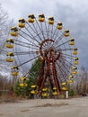 A deserted Ferris wheel surrounded by bare trees under a cloudy sky