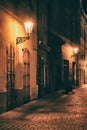 deserted night lane in the old town with a paved sidewalk and street lamps on the walls and a beggar begging, kneeling. analog
