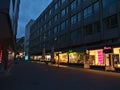 Deserted shopping street with row of closed stores during Covid-19 lockdown and illuminated shop windows in Christmas season.