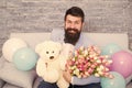 She deserve all best. Romantic man with flowers and teddy bear sit on couch with air balloons waiting girlfriend