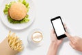 Design concept of mockup using smartphone with burger, french fries and coffee set on white background. Royalty Free Stock Photo
