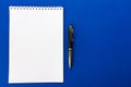 Top view of a spiral school notebook and pens collection on a blue background for layout