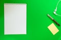 Top view of a spiral school notebook, pens and headphones collection on green background for mockup